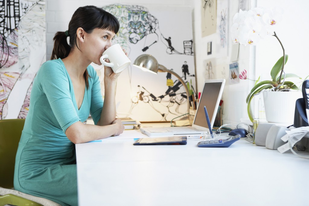 Side view of young businesswoman drinking coffee at office desk